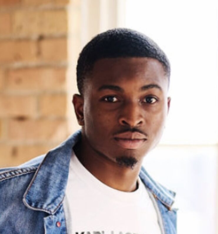 Headshot of Brandon Flowers Kenol, looking straight forward with a white shirt and jean jacket.