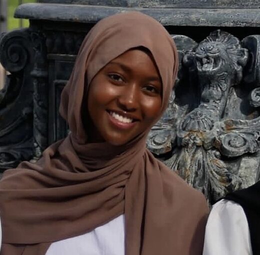 Headshot of Fartun Hassan, smiling in a brown hijab and white shirt.