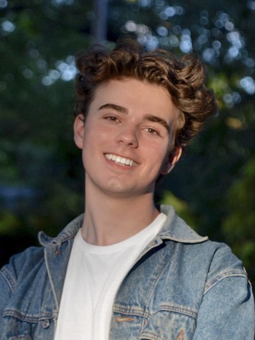 Headshot of Logan Roach, smiling in a white shirt and jean jacket.