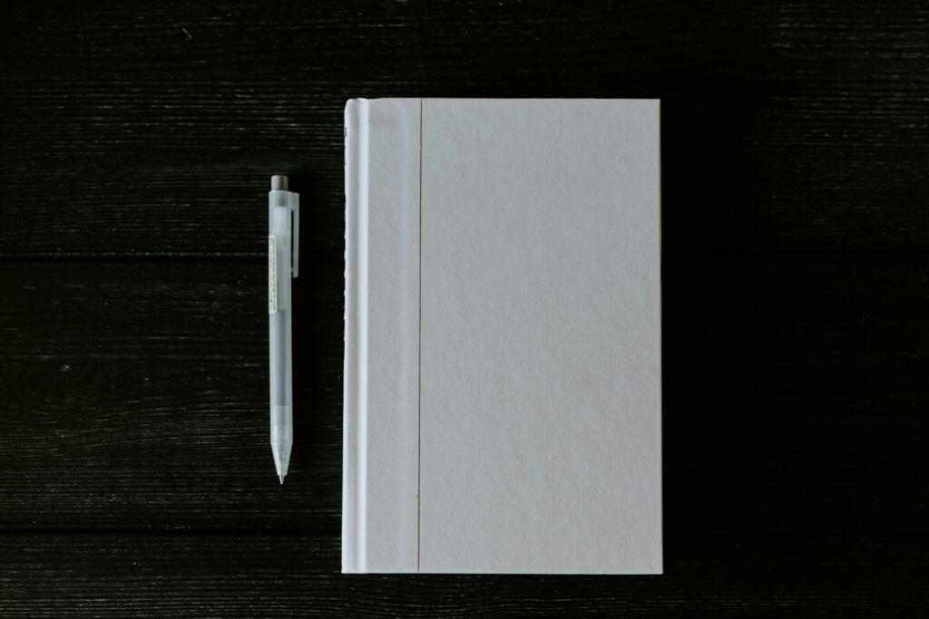 A grey journal and pen rest on a black wooden surface