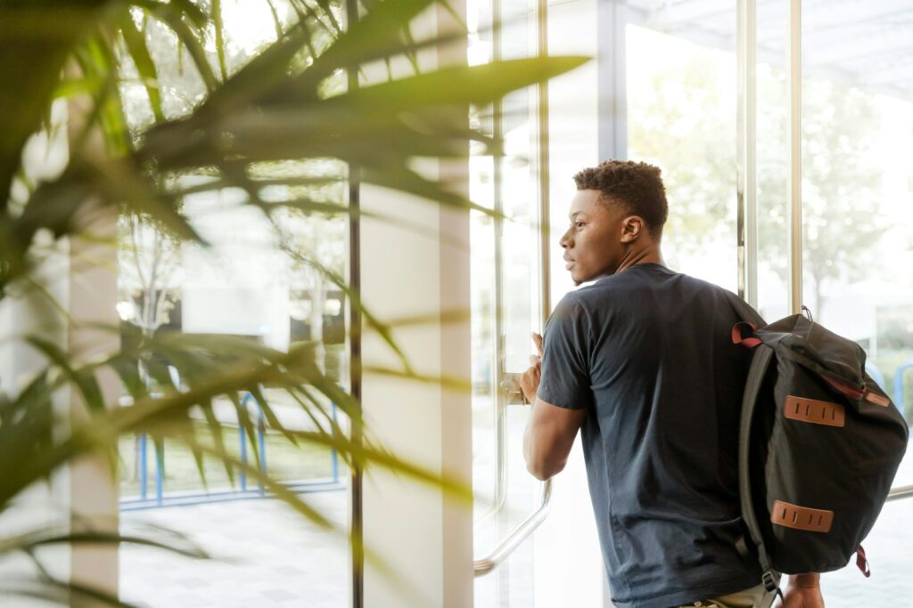 Photo of a student with a black backpack walking out a door