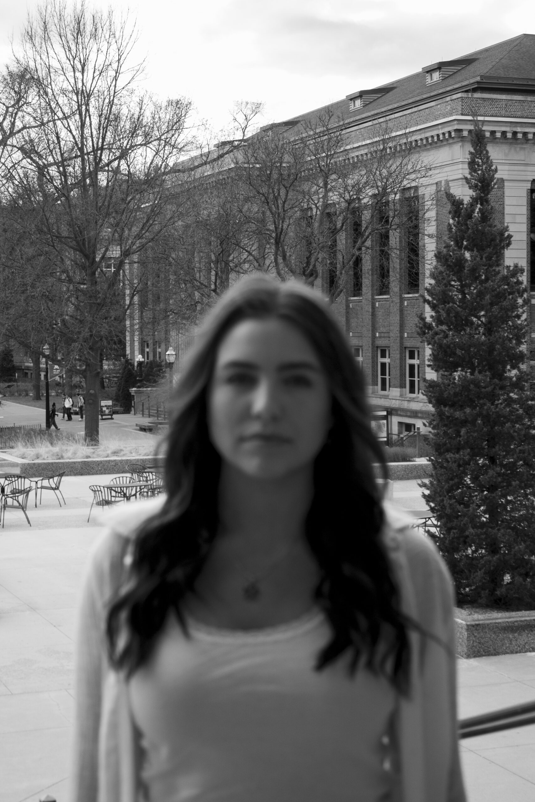 A black and white image of a woman standing on a plaza looking at the camera. She is blurry and the background is in focus.