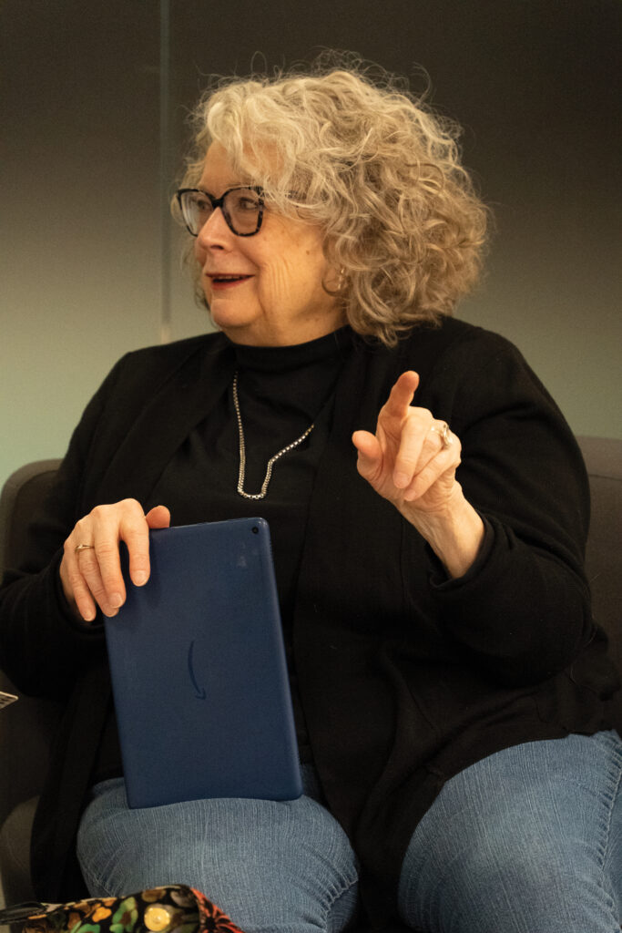 A woman looks to the left, smiling, while holding an iPad in her lap. She points off to the distance with her free hand.